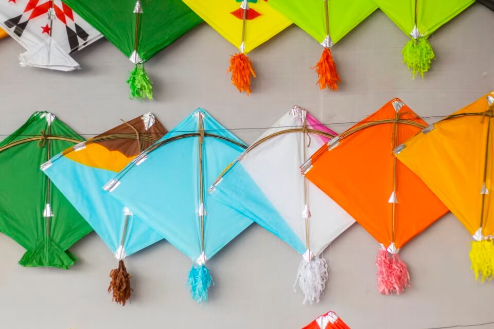 A photograph of a series of brightly coloured, handmade kites, lay flat on a surface.